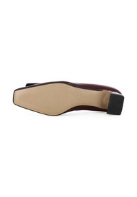 Scarpa piatta borgogna con punta arrotondata, parte superiore in vernice lucida, suola beige texturizzata e tacco quadrato nero.