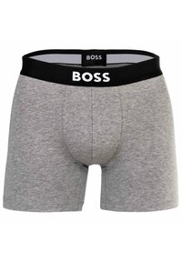 Grå bomullsboxershorts med svart elastiskt midjeband som har varumärkesnamnet "BOSS" i vita bokstäver. Slät textur och åtsittande design.