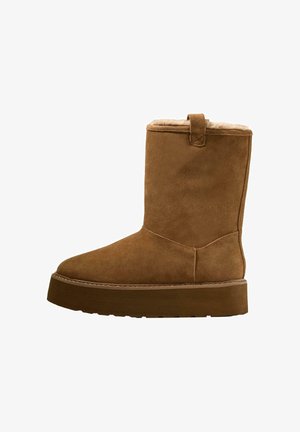 Stivaletto in suede marrone con punta arrotondata, morbida fodera interna e suola piatta spessa. Presenta un piccolo linguetta sul retro.