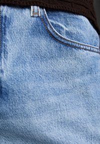 Jasnoniebieskie dżinsy z denimu z efektem sprania, ozdobione pomarańczowym przeszyciem i klasycznym wzorem kieszeni.