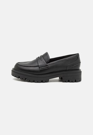 Mocassins en cuir noir avec un bout rond, une semelle en caoutchouc crantée et deux accents cousus sur le dessus pour plus de détails.