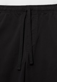 Černé kalhoty s elastickým pasem a černými šňůrkami zavěšenými uprostřed přední části.