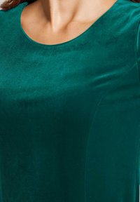 Grünes Samtoberteil mit glatter Textur, rundem Ausschnitt und tailliertem Design. Der Stoff hat eine satte, dunkle Farbe mit einem dezenten Glanz.
