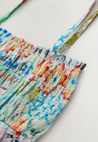 Sac en tissu coloré et à motifs avec une texture froncée, comportant des bretelles bleues et vertes. Des formes florales et géométriques distinctes semblent s'entrelacer.