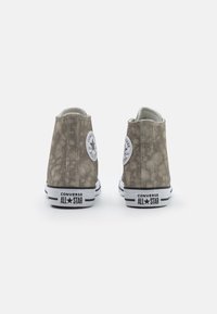 Gray high-top sneakers with a textured upper, white rubber sole, and circular logo patch featuring a star. Black contrasting stripes along the sole.