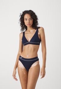 Navy blue bikini set featuring a v-neck bralette with wide straps, a contrasting white trim, and matching high-waisted brief with logo.