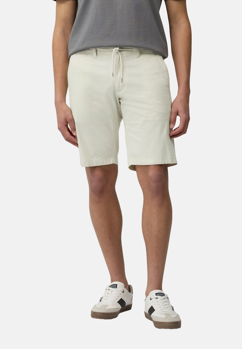 Helle beigen Shorts mit einem Kordelzugbund, aus weichem Stoff, mit Seitentaschen und einer entspannten Passform, kombiniert mit weißen Sneakers.