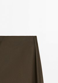 Donkerbruine stof gedrapeerd tegen een eenvoudige witte achtergrond met een gladde textuur en lichte plooien aan de rechterkant.