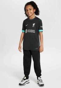 Svart Liverpool FC-tröja med turkosa detaljer, korta ärmar och logotyp, i kombination med svarta joggers och svarta och vita träningsskor.