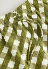 Gros plan du tissu d'un short à carreaux verts et beiges avec un motif texturé et une ceinture à cordon.