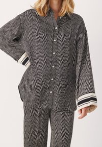 Chemise à boutons en noir et blanc avec un motif en chevrons, à coupe décontractée et avec des poignets rayés contrastants, fabriquée dans un tissu léger.