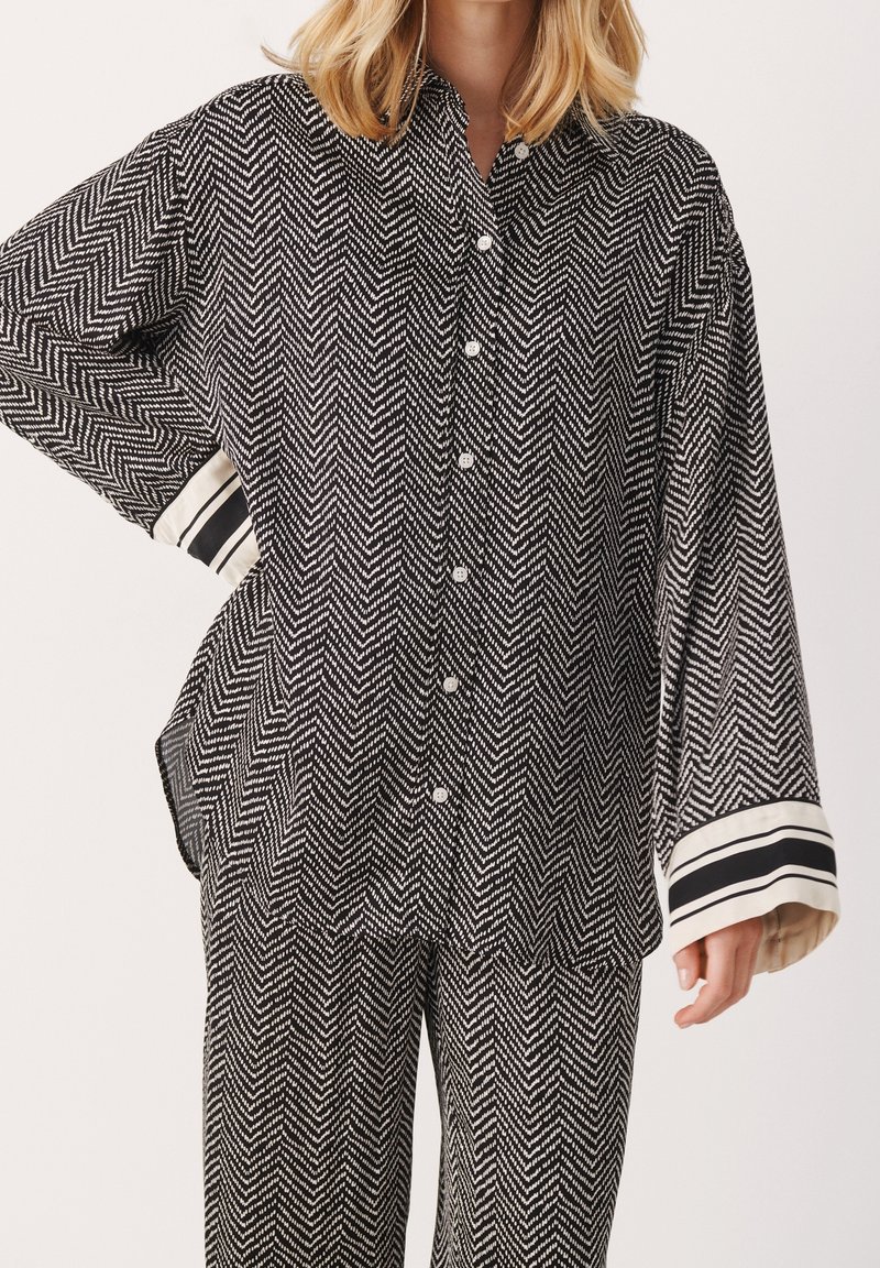 Chemise à boutons en noir et blanc avec un motif en chevrons, à coupe décontractée et avec des poignets rayés contrastants, fabriquée dans un tissu léger.