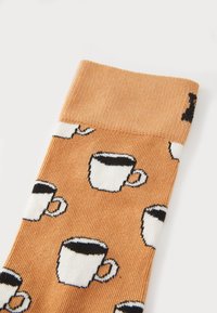 Orange socks with a textured ribbed pattern featuring small white coffee cup illustrations, with black detailing around the rims.