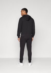 Hoodie noir et jogging en tissu doux, design ajusté avec des poignets côtelés et une poche kangourou à l'avant. Baskets blanches.