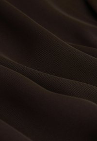 Dunkelbrauner Stoff mit feiner gerippter Textur und weichen Falten, die sanfte Wellen über die Oberfläche erzeugen.