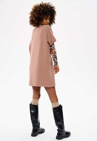 Oversize różowa sukienka z krótkimi rękawami, miękki materiał i prosty krój. W połączeniu z czarnymi kozakami do kolan i pasiastymi skarpetkami.