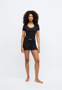 Black short-sleeve top with a scoop neckline paired with black shorts featuring an elastic waistband and subtle brand logo detail.