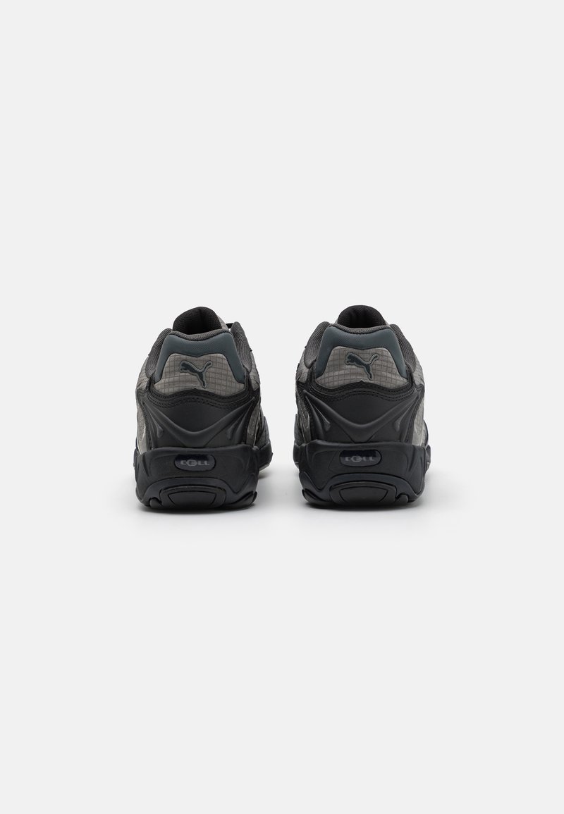 Schwarze und graue Sportschuhe mit Obermaterial aus Mesh, gepolsterter Sohle und auffälligem Logoschild auf der Rückseite. Dicke, strukturierte Sohle für guten Halt.