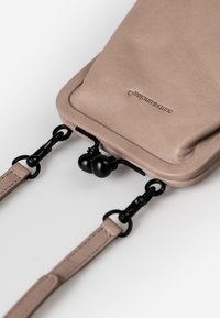 Borsa a tracolla in pelle di un morbido taupe, con accessori neri, cinturini regolabili e una forma arrotondata con un design minimalista.