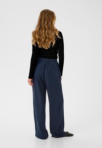 Pantalons large en marine avec un tissu texturé, une taille élastique et une coupe décontractée, associés à un haut à manches longues noir.