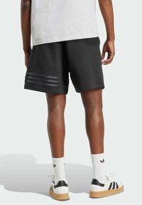 Černé sportovní šortky z měkké látky, s designem tří pruhů na lemu. Spárované s bílými teniskami a žebrovanými ponožkami.