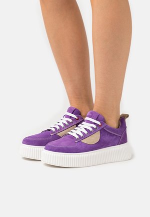 Lila mockasin-sneakers med vita snören och en kontrasterande beige panel. Tjock vit sula med texturerad ribbning för extra grepp.
