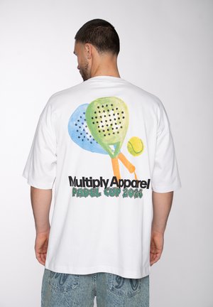 Mann trägt weißes T-Shirt mit bunten Padel-Schlägern, Tennisball und Text „Multiply Apparel Padel Cup 2026“ auf dem Rücken.