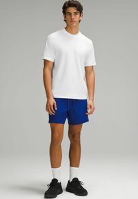 Hvid T-shirt med korte ærmer kombineret med blå shorts. Shortsene har en elastisk talje og er knælange. Sorte træningssko fuldender outfittet.