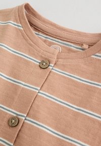 Zbliżenie na jasnobrązową koszulę w paski z białymi i szarymi poziomymi paskami oraz dwoma brązowymi guzikami przy kołnierzyku.