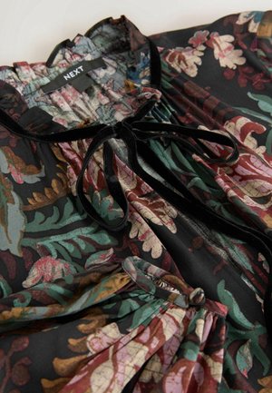 Bluzka w kwiatowy wzór z ciemnozielonymi, czerwonymi i beżowymi liśćmi, z czarną aksamitną kokardą przy marszczonym dekolcie.