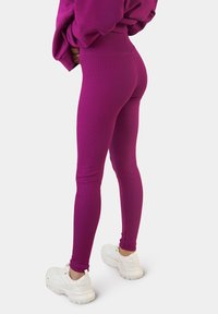 Strakke leggings van levendig paarse stof, met een gladde textuur en hoge taille. Gecombineerd met witte sportschoenen voor contrast.