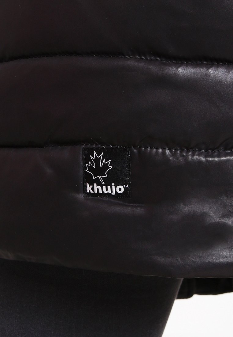Sort pufferjakke lavet af skinnende stof. Har et kviltet design og et sort mærke med et hvidt ahornblad og mærkenavnet "khujo."