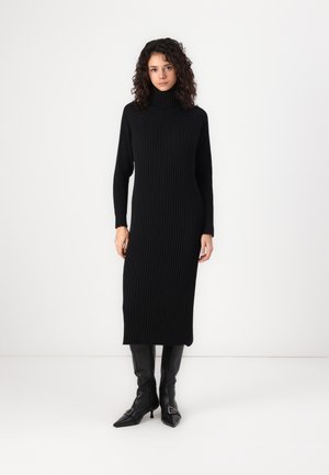 Black ribbed knit dress with a high collar, long sleeves, and side slits, worn with knee-high black pointed-toe boots.