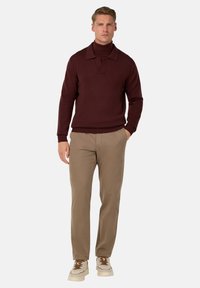 Maglione polo a maglia bordeaux con colletto, abbinato a pantaloni beige e sneakers bianche con accentuazioni marroni. Texture liscia in tutto.