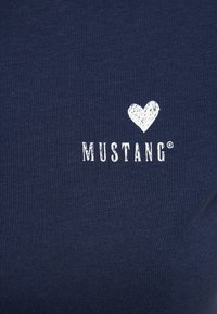 Tmavě modré bavlněné tričko s bílým srdcem a textem "MUSTANG" v texturovaném, opotřebovaném písmu. Hladký povrch s krátkými rukávy.