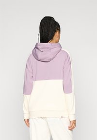 Φούτερ με κουκούλα σε λιλά και κρέμα. Μαλακό ύφασμα με σχέδιο σε χρωματική μπλοκ, διαθέτει μπροστινή τσέπη καγκουρό και ριμπ μανσέτες.