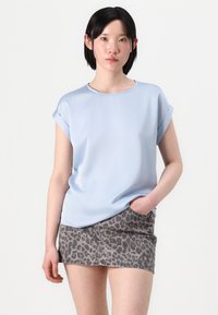 Top blu chiaro a maniche corte con scollatura rotonda, abbinato a una mini gonna grigia con stampa leopardata. Tessuto morbido, vestibilità casual.
