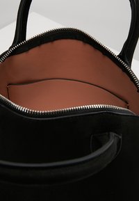 Sort ruskindstaske med en glat brun inderside, lynlås lukning og to håndtag. Den har et rummeligt hovedrum og en slip-lomme.