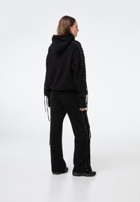 Czarna bluza z kapturem z koronkowymi akcentami na rękawach, zestawiona z czarnymi spodniami z koronkowymi detalami wzdłuż boków. Gładka faktura.