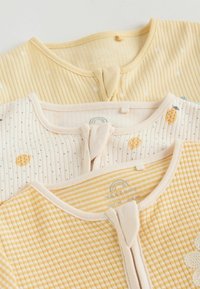 Trys sulankstyti kūdikių kombinezonai geltonų atspalvių, su kirptu, dryžuotu ir vaisių raštuotomis tekstūromis, priekyje su užtrauktukais.