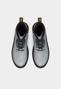 Ζευγάρι ασημί-γκρι μπότες με κορδόνια, μαύρες σόλες και πορτοκαλί ραφές, φωτογραφημένες από πάνω σε απλό λευκό φόντο.