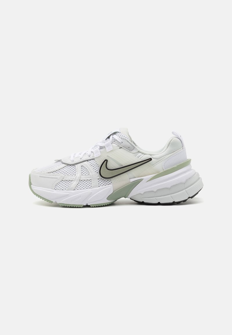 Bijela atletska cipela s mrežastim i sintetičkim materijalima. Ima crni Swoosh logo, debelu potplatu s zelenim akcentima i zatvaranje na vezice.