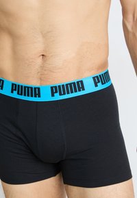 Schwarze Boxershorts mit einem hellblauen Gummibund, der mit schwarzen "PUMA"-Buchstaben bedruckt ist. Der Stoff wirkt glatt und hat eine figurbetonte Passform.