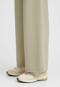 Pantalones de pierna ancha en beige claro, fabricados con un tejido suave, combinados con unas zapatillas deportivas en beige y gris que presentan detalles de malla y goma.