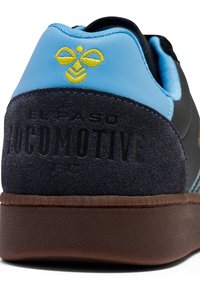 Sapatilha preta e azul com um calcanhar de camurça texturizada, logótipo amarelo bordado e sola de borracha castanha. Apresenta o texto “EL PASO LOCOMOTIVE FC”.}}}### Output:  {