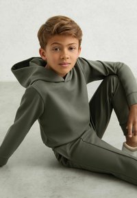Olivengrøn hættetrøje og matchende sweatpants lavet af blødt stof. Hættetrøjen har et klassisk design med en kengur lomme.