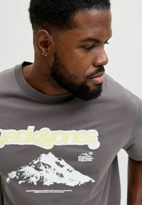 Siva bombažna majica z belečo grafiko gore in rumenim logotipom "jack&jones". Kratki rokavi in okrogel izrez.