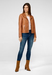 Bruine leren motorjack met een rits, een schuine kraag en ritszakken, gecombineerd met strakke jeans en bruine haklaarzen.
