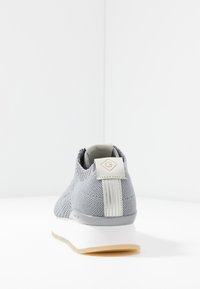 Baskets tricotées grises avec une semelle blanche, présentant une tige texturée, un accent logo sur le talon et un détail rayé à l'arrière.