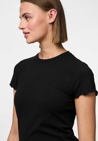 T-shirt noir à côtes avec des manches courtes à bords ondulés et un col rond. La texture lisse et le design ajusté mettent en valeur la silhouette.